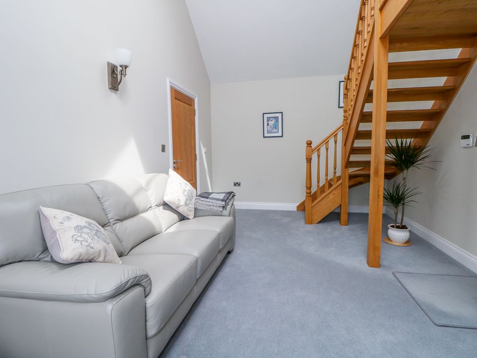 A living room with a light gray sofa wooden stairs and a potted plant at Thistledown Cottage in Chidham near Bosham