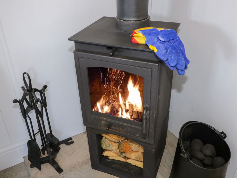 A wood burning stove with fire inside gloves on top fire tools on the left and a black container with coal on the right at High Rigg Shepherd's Retreat in Brampton Cumbria