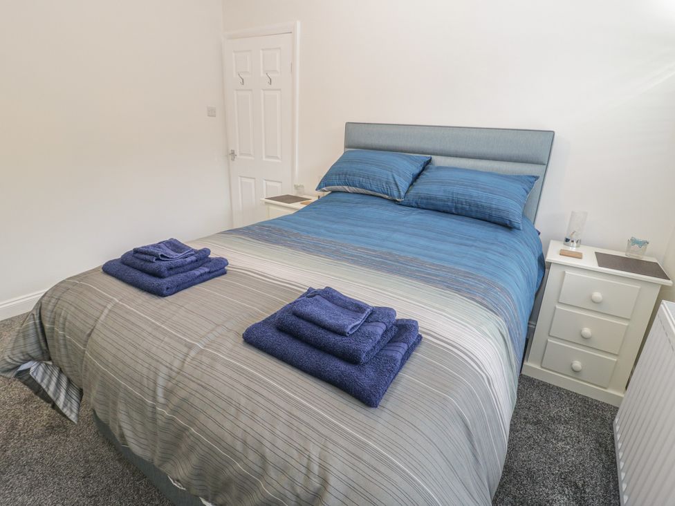 A bedroom with a bed with blue and gray striped bedding two nightstands with lamps and folded towels on the bed at The Nook in Colwyn Bay