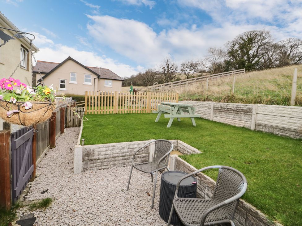 A garden area with two chairs and a table on a gravel path and a picnic bench on grass at The Nook in Colwyn Bay