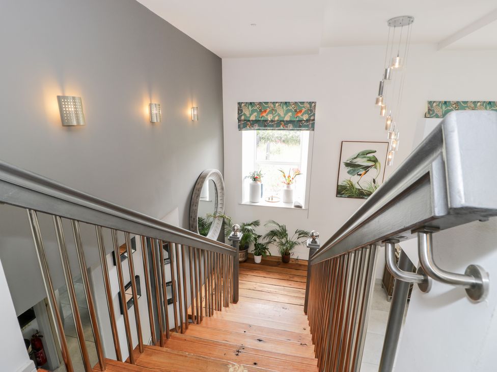 A staircase with wooden steps metal railings plants under a window and wall lights at Capel Mawr Basement 19 in Llanrug