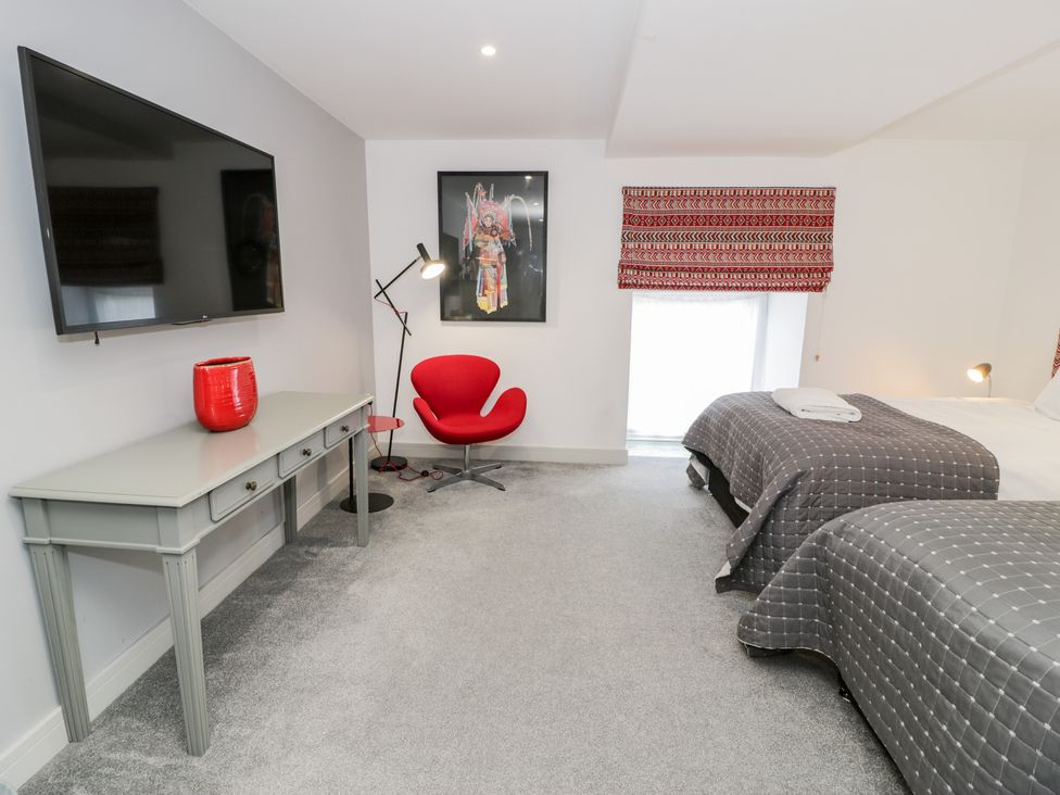 A bedroom with two beds a gray desk a red chair and wall-mounted tv at Capel Mawr Basement 19 Llanrug