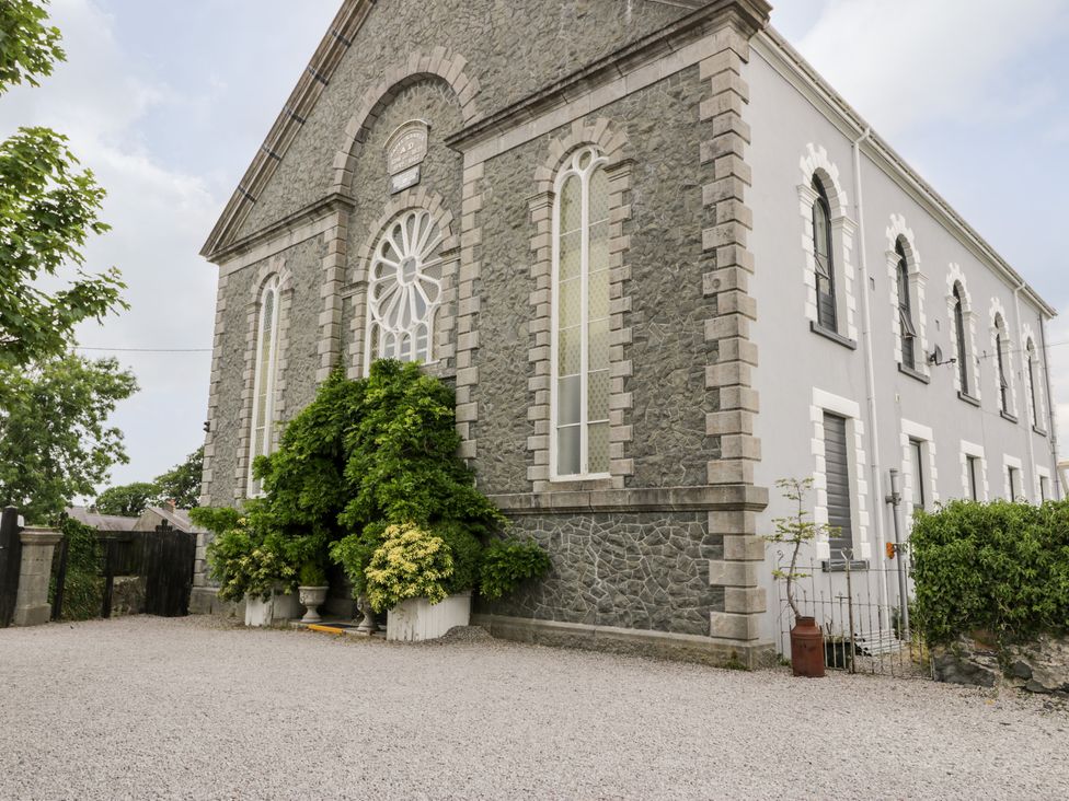 Exterior stone and stucco building with arched windows and greenery at Capel Mawr Basement 19 in Llanrug