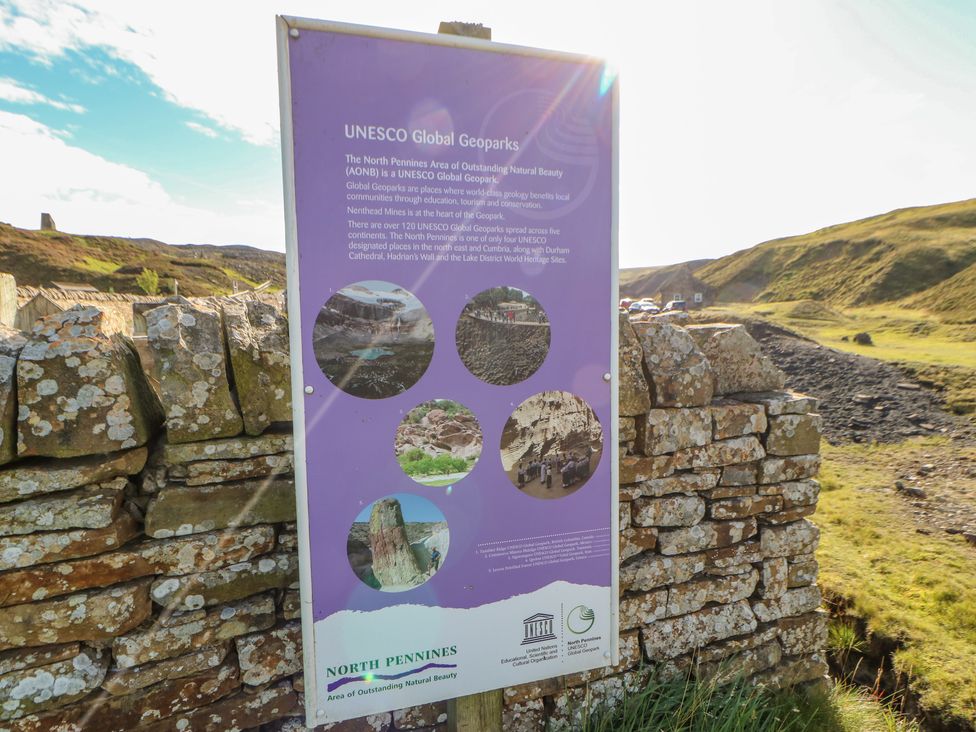 An outdoor information sign about UNESCO Global Geoparks mounted on a stone wall in a rural landscape at Field Barn in Alston