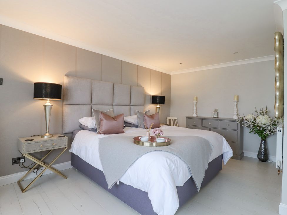 A bedroom with a large bed with pillows and blankets two bedside tables with lamps a dresser with candles and flowers a chair and a vase with flowers at Closefield in Ivinghoe Aston near Ivinghoe