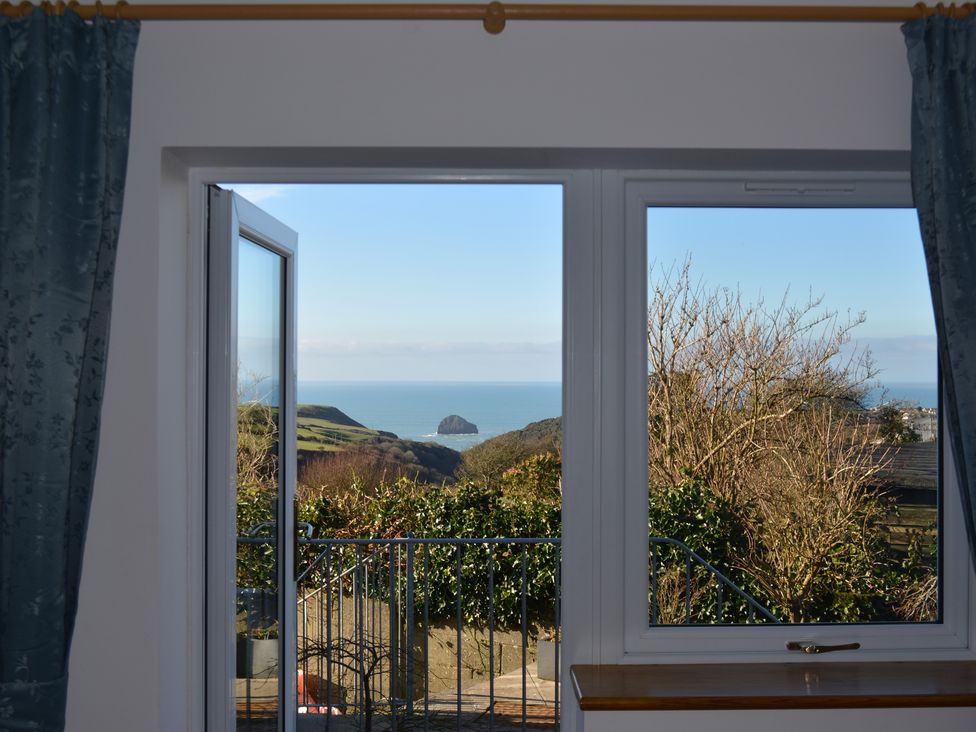 A window and door open to a balcony with a view of trees hills and the sea at Glenhaven in Trewarmett near Tintagel