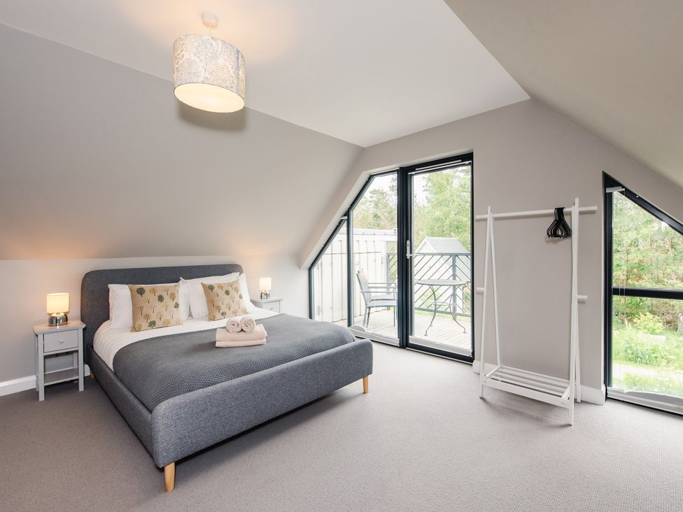 A bedroom with a gray bed and two bedside tables near large glass doors opening to a balcony at Golden Eagle Lodge in Aviemore