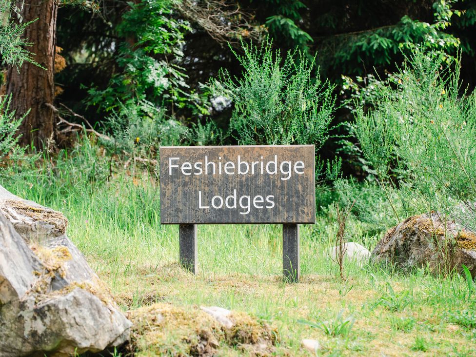 A sign reading Feshiebridge Lodges surrounded by grass rocks and trees at Golden Eagle Lodge in Aviemore