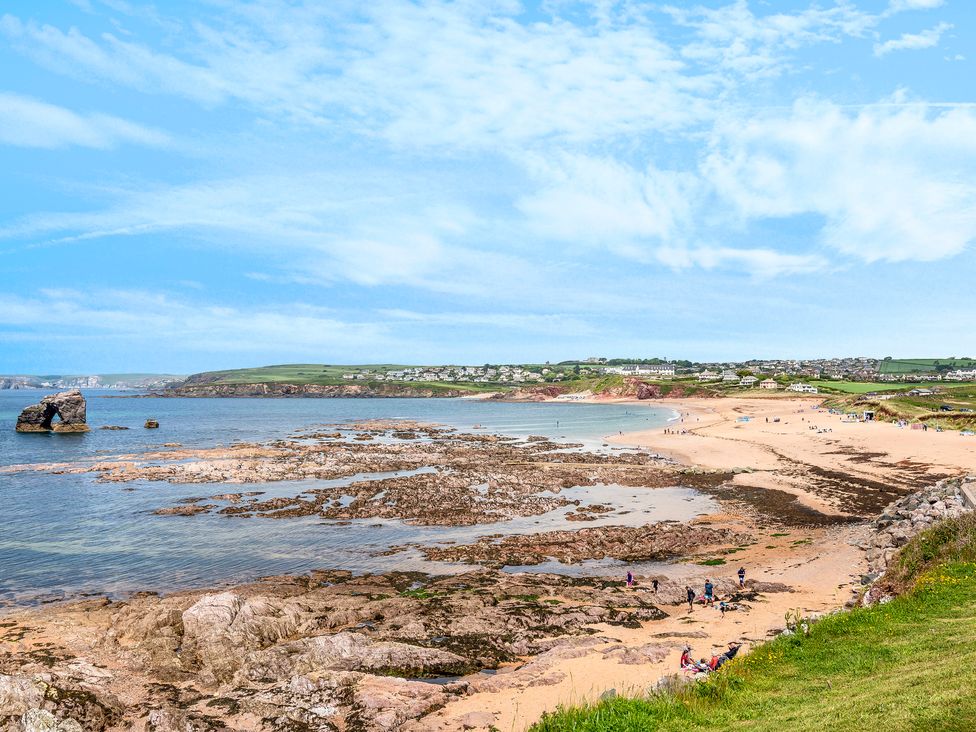 A beach with rocky shore and people near the water with houses and green hills in the background at 7 Ocean's Edge in Thurlestone