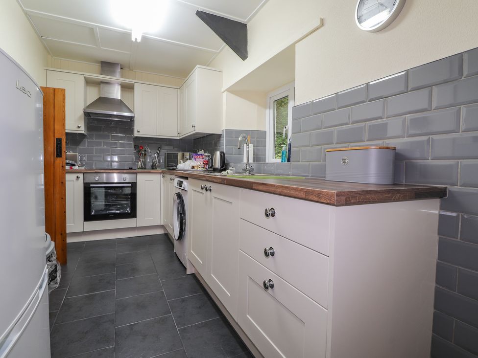 A kitchen with white cabinets gray tiled backsplash a stainless steel oven and range hood a washing machine and a white refrigerator at Panteg Cardigan in Llangoedmor Cardigan