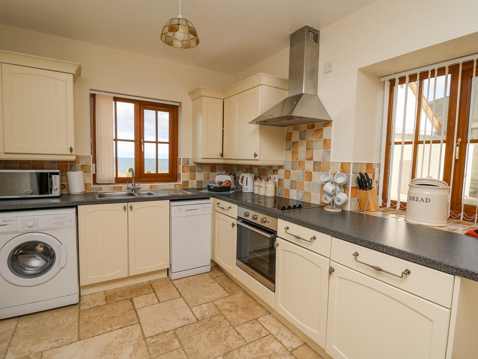 A kitchen with cream cabinets washing machine dishwasher oven and windows at Beudy in Mwnt Cardigan Ceredigion