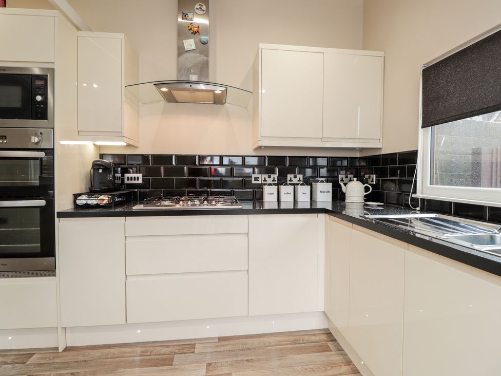 A kitchen with white cabinets black tiled backsplash a gas stove coffee machine canisters and a window with a black blind at Sparrows Den Lodge in Winchelsea Beach