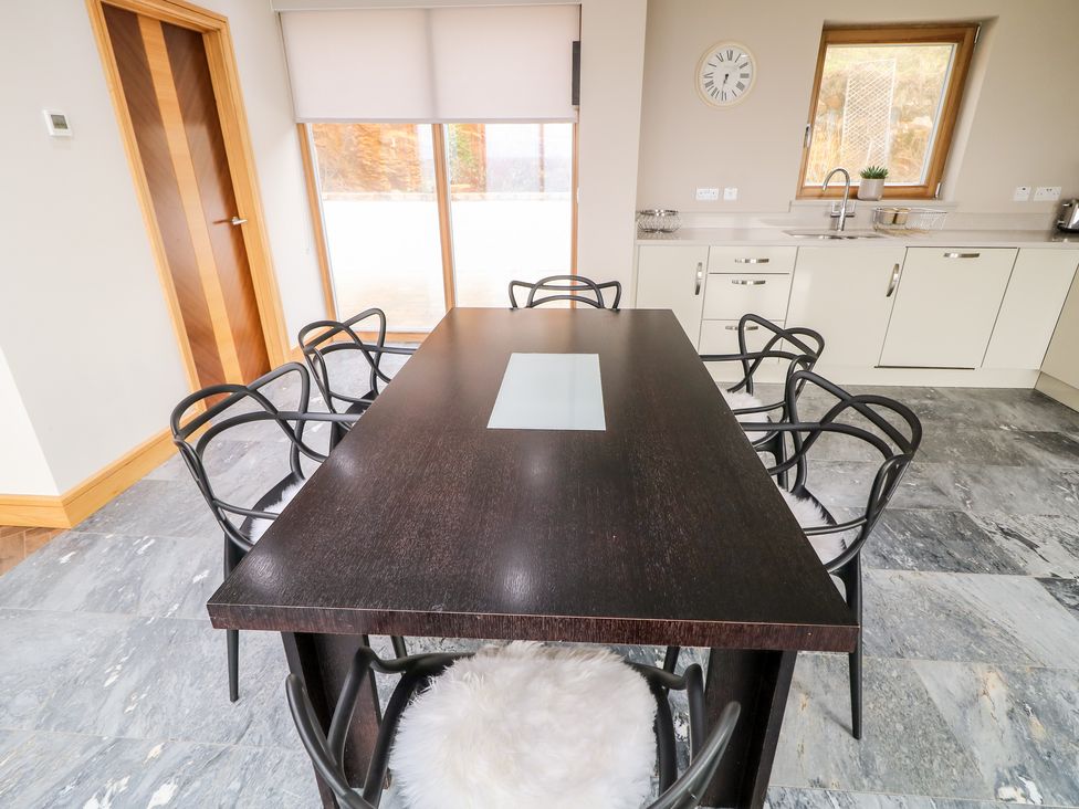 A dining area with a dark rectangular table and six black chairs with white cushions in a kitchen at House Crohy Head in Dungloe County Donegal