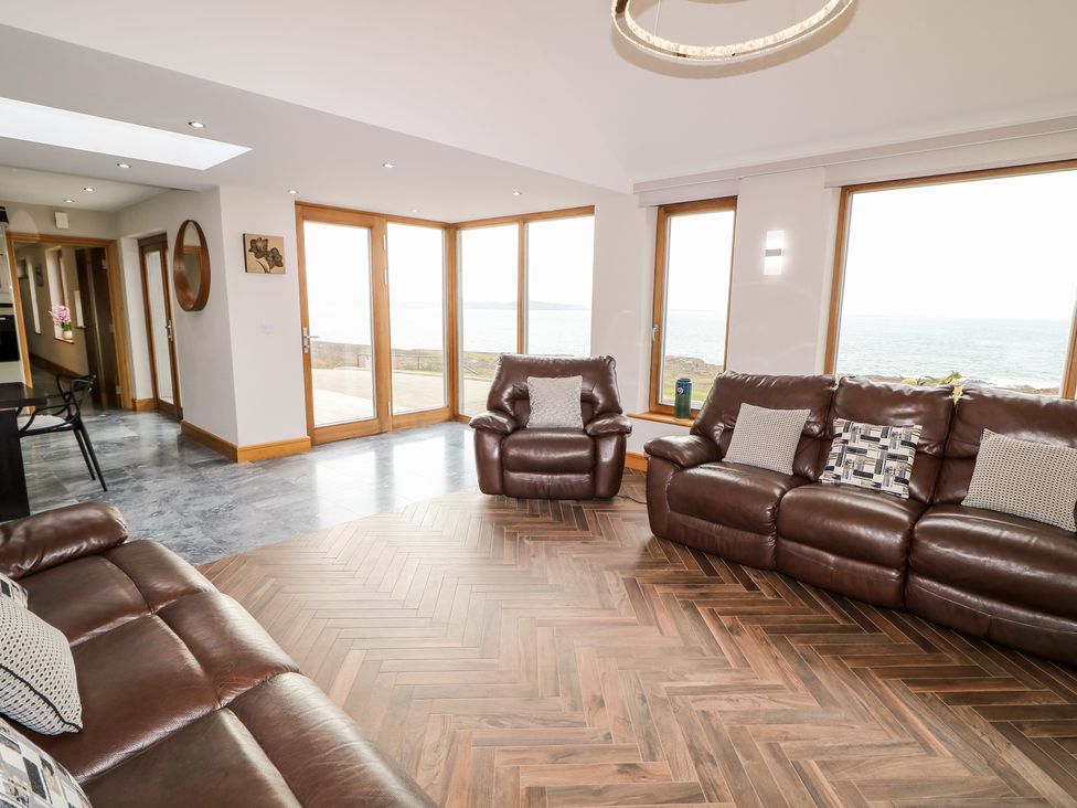 A living room with brown leather sofas and armchair and large windows showing a sea view at House Crohy Head in Dungloe County Donegal