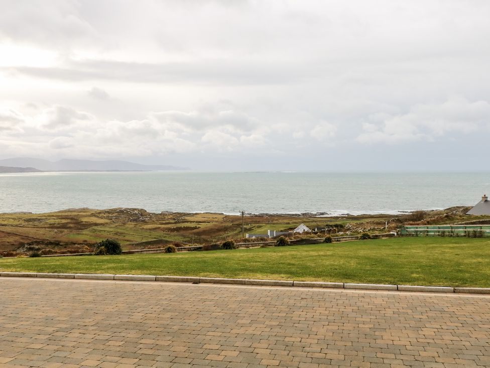 A paved driveway and green lawn overlooking a coastal landscape with the sea and distant hills at House Crohy Head in Dungloe County Donegal