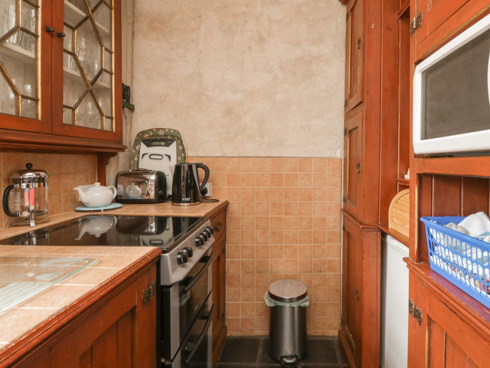 A small kitchen with wooden cabinets a stove toaster electric kettle and a microwave at The Pend in Whithorn