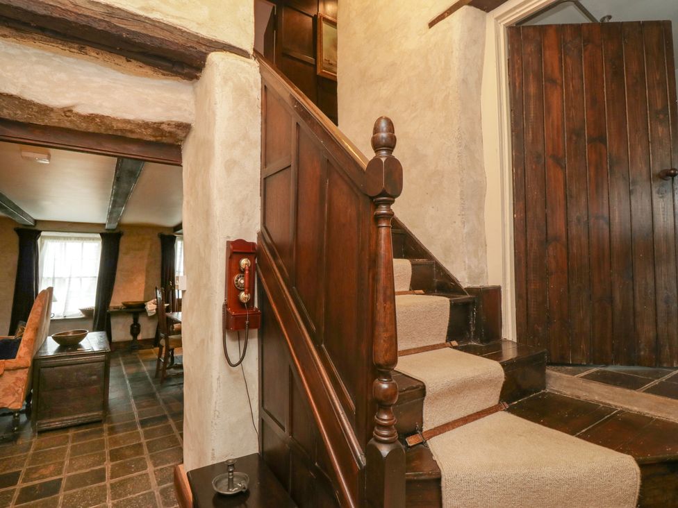 A staircase with carpet runners and a wooden railing next to a wall-mounted vintage telephone in a room with wooden furniture and stone flooring at The Pend in Whithorn