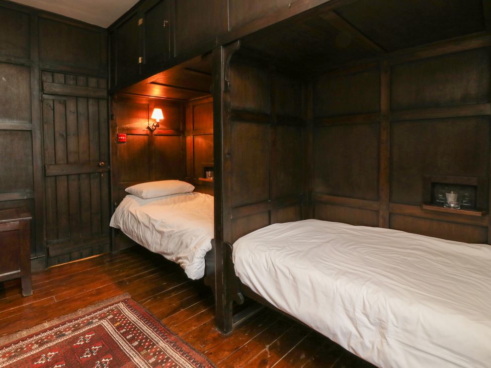A bedroom with two single beds and dark wooden paneling at The Pend in Whithorn
