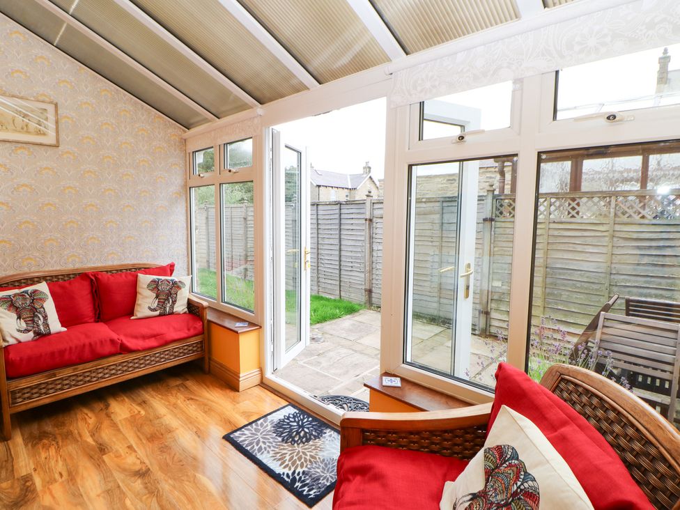 A conservatory with wicker sofas with red cushions and elephant print pillows at Langlands in Middleton-In-Teesdale