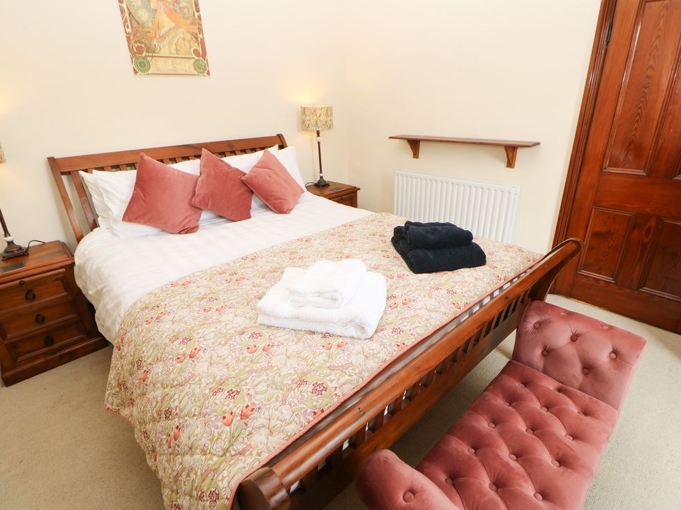A bedroom with a wooden bed with pillows and folded towels a pink cushioned bench and wooden furniture at Langlands in Middleton-In-Teesdale