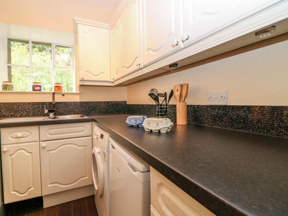 A kitchen with white cabinets a black countertop a sink a washing machine and utensils at Gardener's Cottage Noranside near Kirriemuir