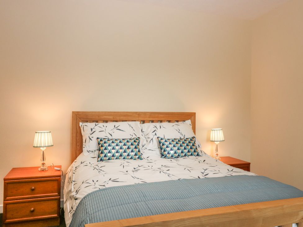 A bedroom with a wooden bed frame bedside tables lamps and patterned bedding at Gardener's Cottage in Noranside near Kirriemuir