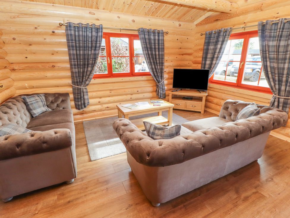 A living room with two sofas a wooden coffee table a TV on a stand and windows with curtains at Maple Lodge in Greetham Rutland