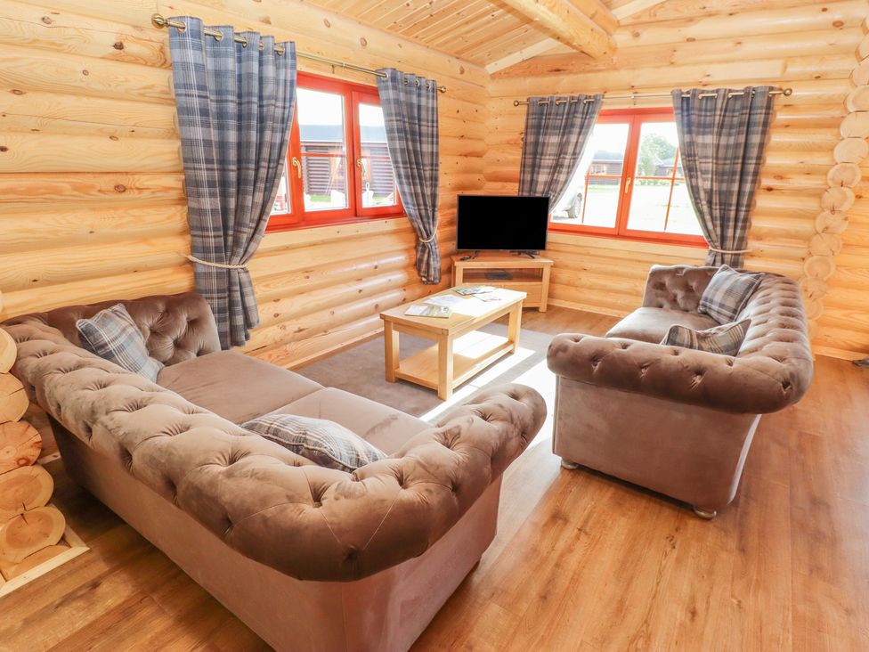 A living room with two sofas a coffee table a television and windows with plaid curtains at Maple Lodge in Greetham Rutland