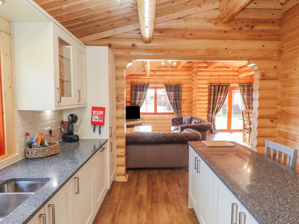 A kitchen with countertops and cabinets leading to a living area with sofas and windows at Maple Lodge in Greetham Rutland