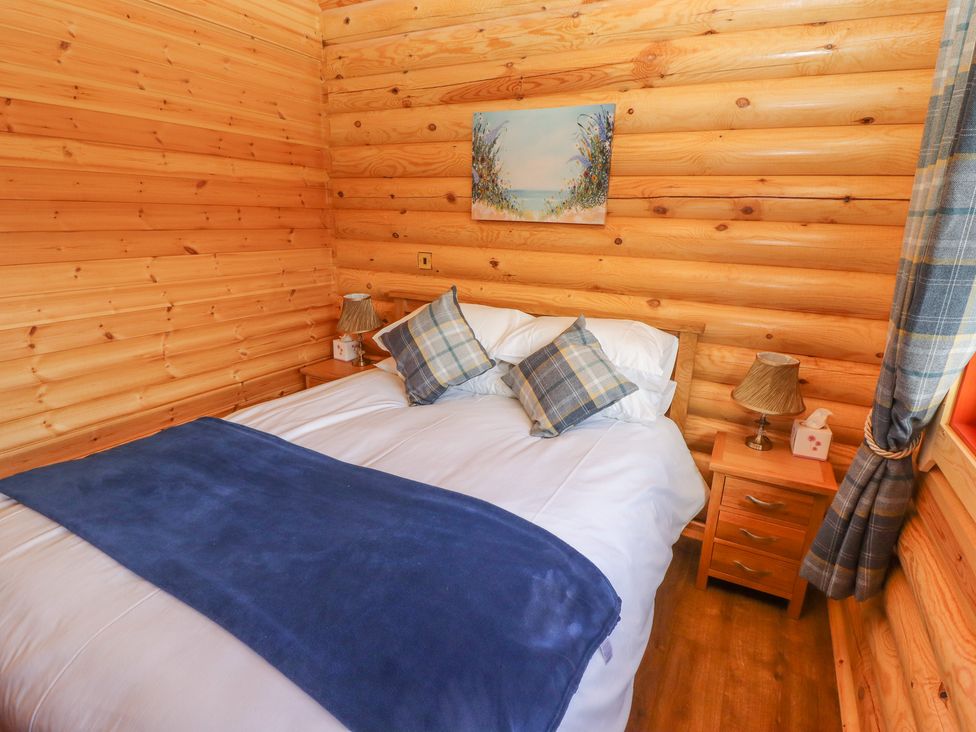 A bedroom with wooden walls a double bed blue blanket and two bedside tables at Maple Lodge in Greetham Rutland