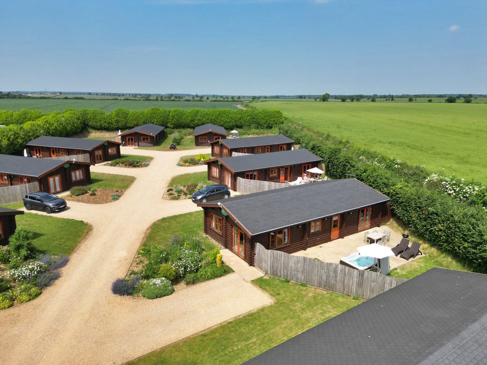 A cluster of wooden lodges with gardens and parked cars in a rural area at Maple Lodge in Greetham Rutland