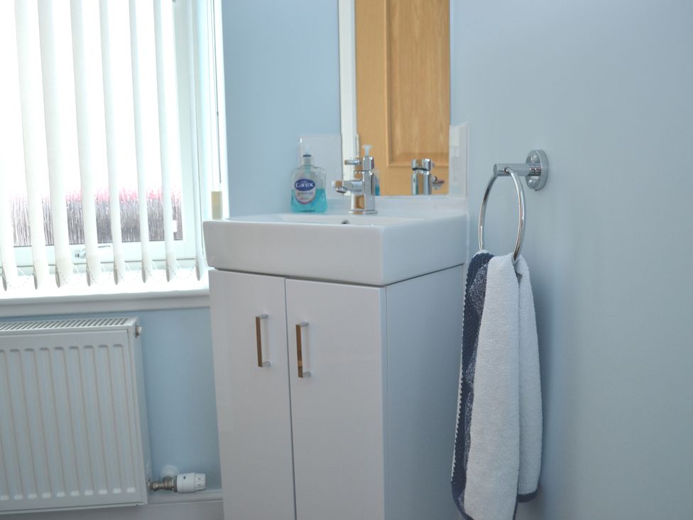 A bathroom sink with a mirror a towel ring and a window with vertical blinds at Tammie Norrie Cottage in Banff