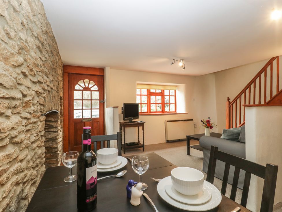 A living and dining area with a dining table set with plates and wine and a couch near stairs at Jasmine Cottage in South Perrott near Mosterton
