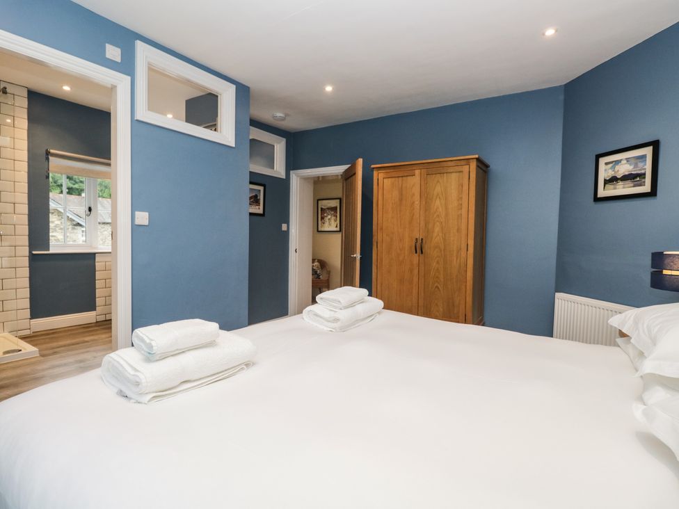 A bedroom with a white bed and folded towels near a wooden wardrobe and two doorways at Home Farmhouse Graythwaite near Hawkshead