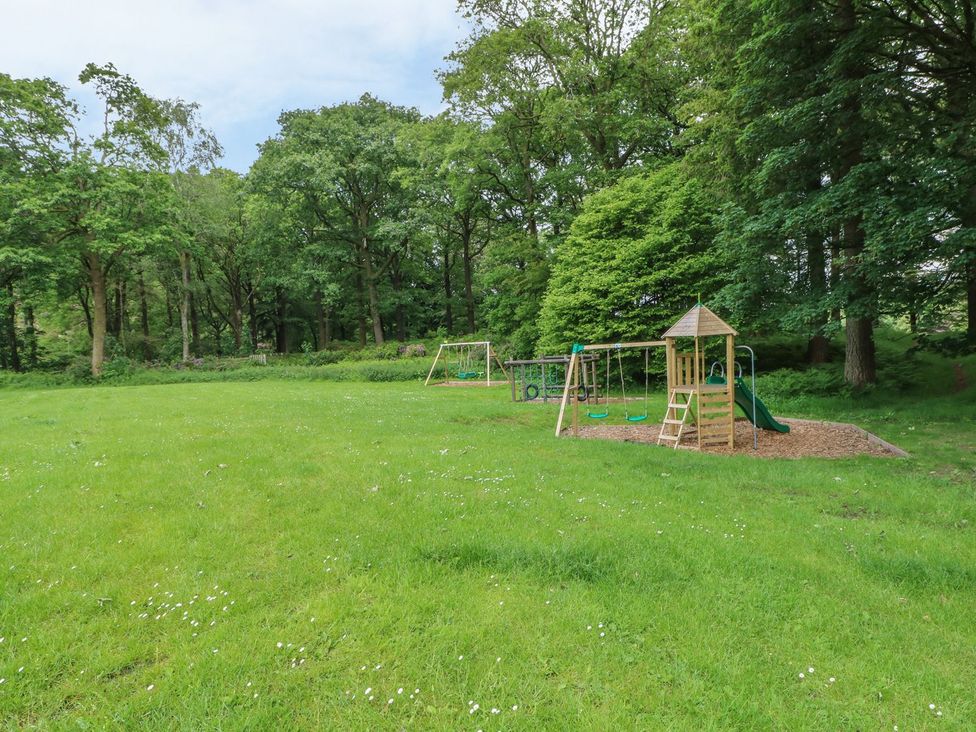 A playground with swings and a slide in a grassy area surrounded by trees at Home Farmhouse Graythwaite near Hawkshead