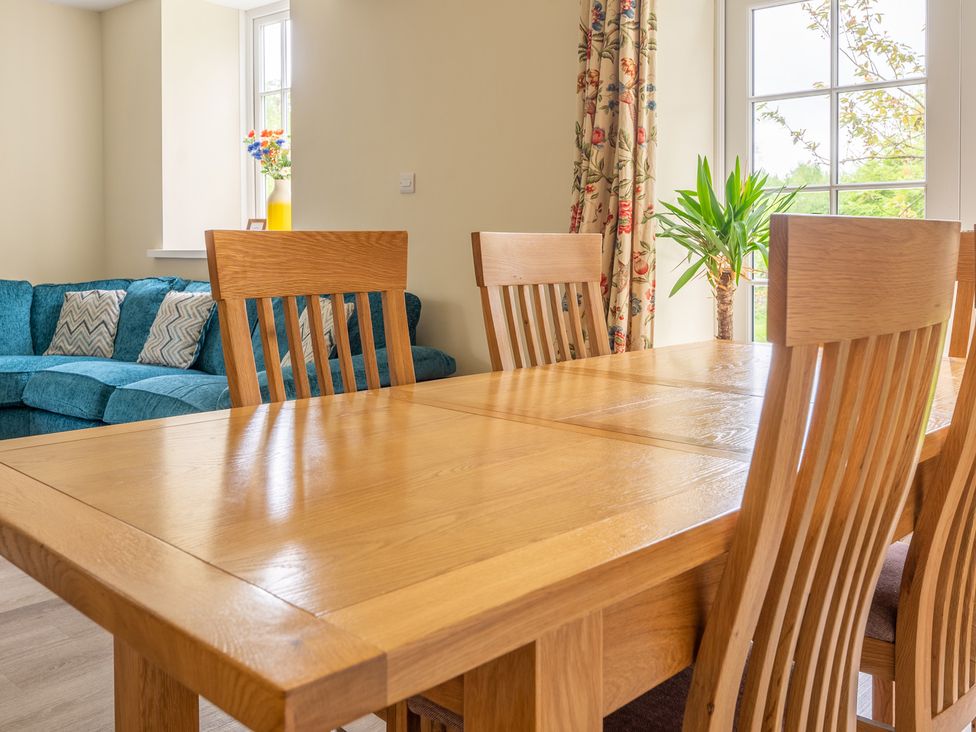 A dining table with wooden chairs next to a window and a blue sofa in the background at Home Farmhouse in Graythwaite near Hawkshead