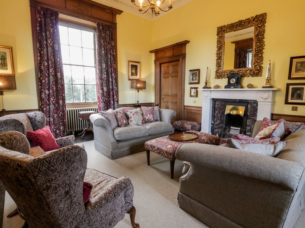 A living room with sofas, armchairs, a fireplace, and floral curtains at Harmony House - Harmony Gardens in Melrose