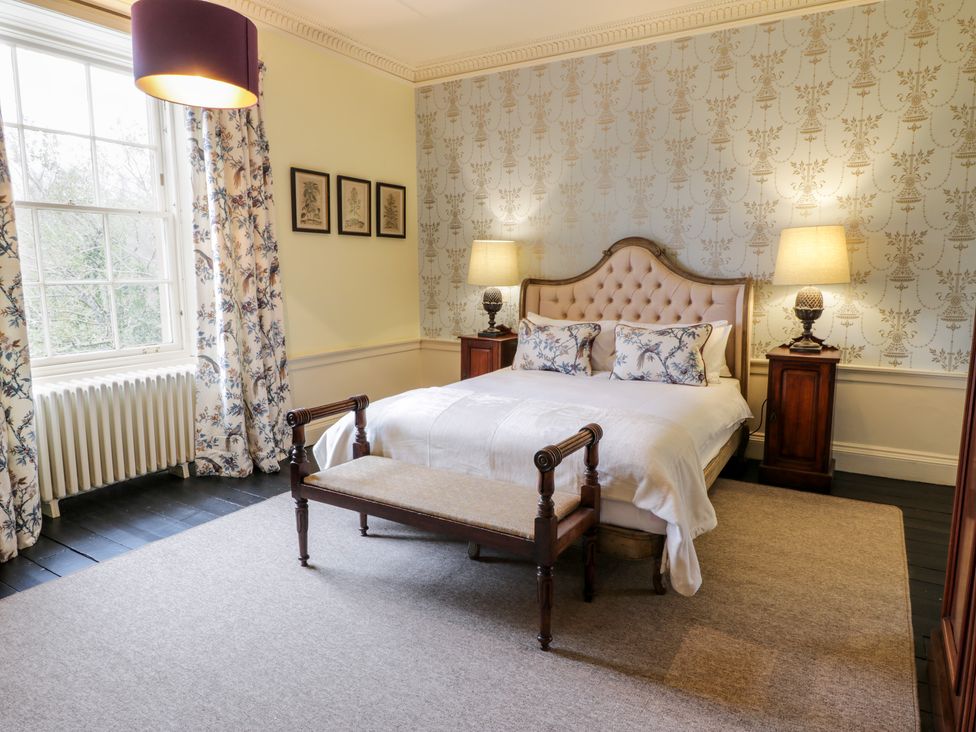 A bedroom with a bed two bedside tables with lamps a bench a window with curtains and three framed pictures on the wall at Harmony House - Harmony Gardens in Melrose