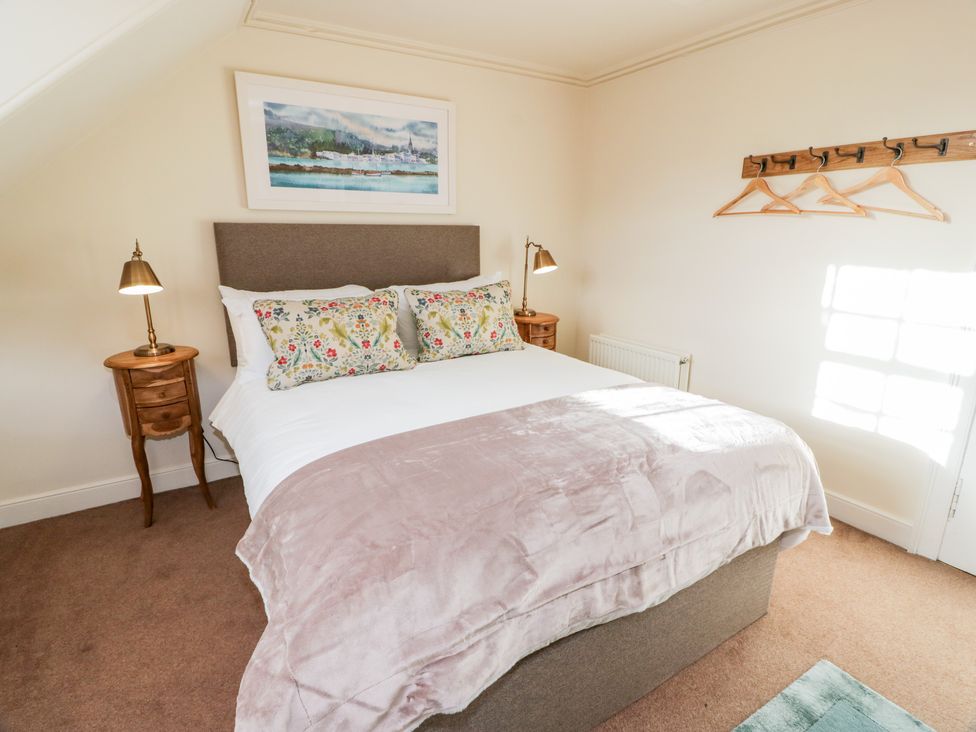 A bedroom with a bed floral pillows side tables lamps wall art and a wooden coat rack at Harmony House - Harmony Gardens in Melrose