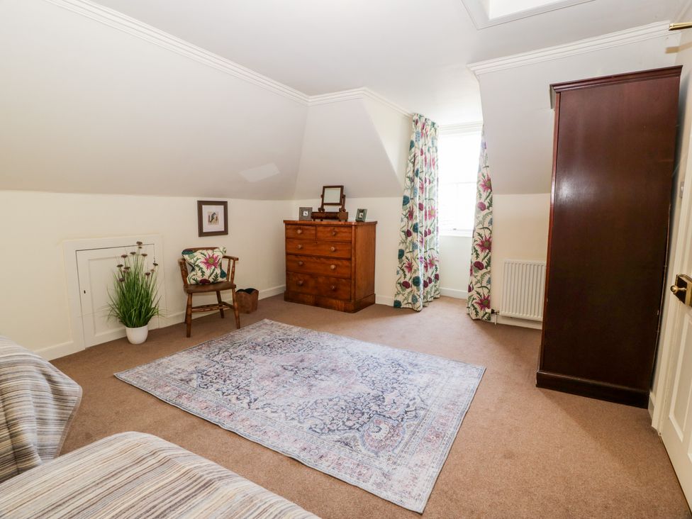 A room with a patterned rug on carpet floor a wooden chest of drawers a wooden chair with a cushion floral curtains and a dark wooden wardrobe at Harmony House Harmony Gardens in Melrose
