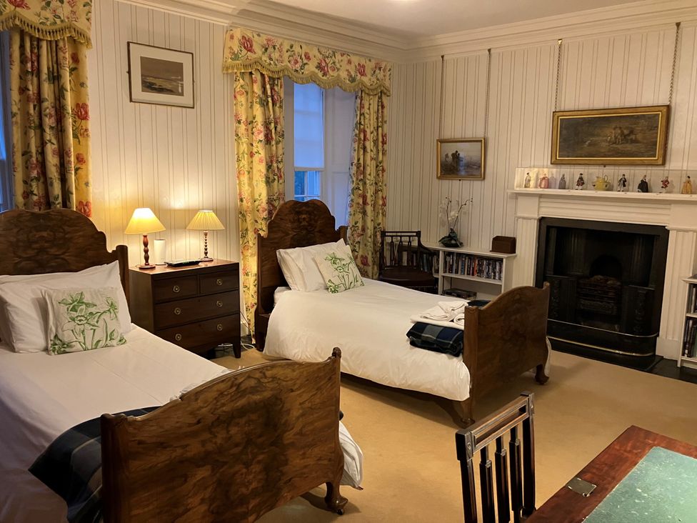 A bedroom with two single beds a wooden chest of drawers two lamps a fireplace and floral curtains at The Lairds Wing Brodie Castle in Forres