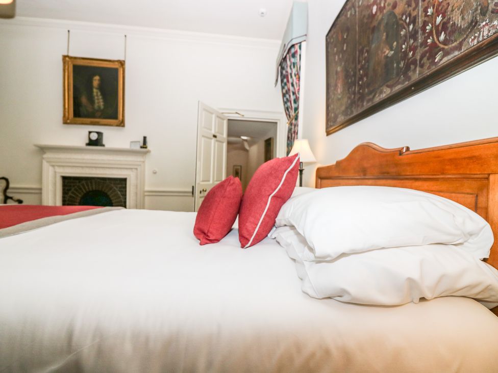 A bedroom with a wooden bed frame white bedding red pillows a fireplace and framed paintings at The Preston Tower Apartment - Fyvie Castle in Rothienorman
