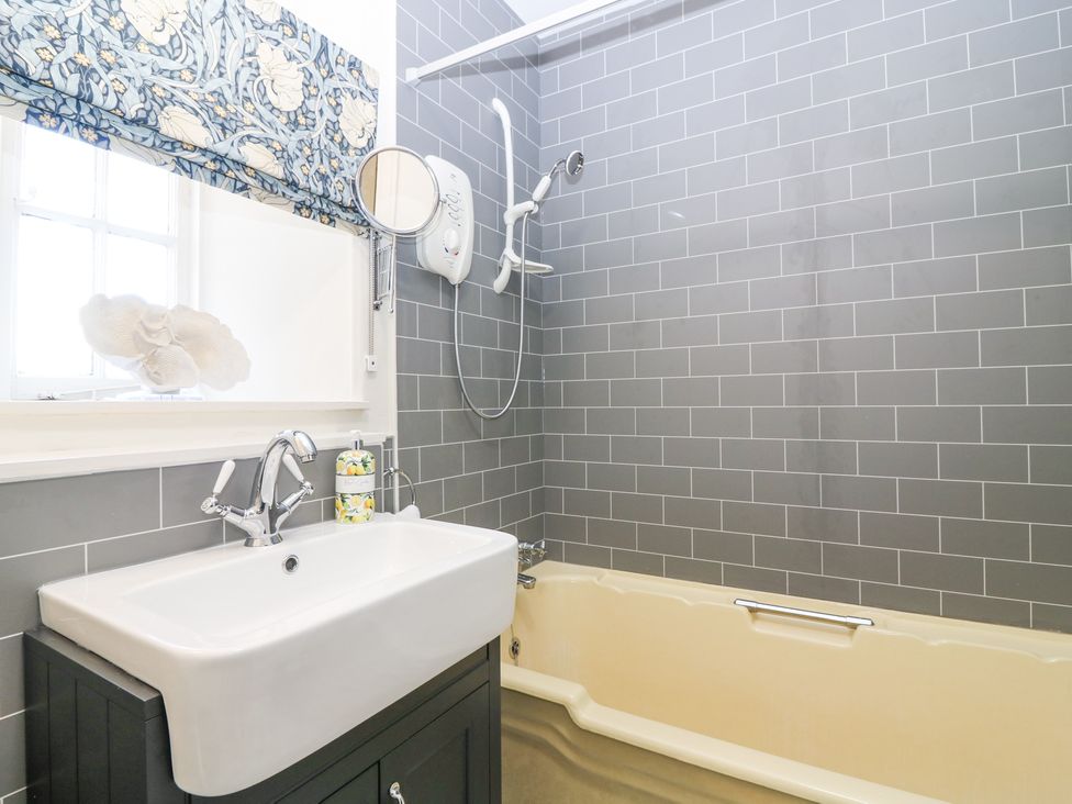 A bathroom with a bathtub a shower a sink with a faucet and a window with a floral curtain at North Wing - Pitmedden Gardens in Pitmedden