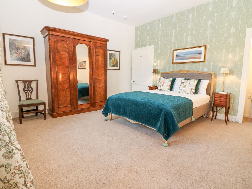 A bedroom with a bed covered with a teal bedspread a wooden wardrobe and a chair at North Wing - Pitmedden Gardens in Pitmedden