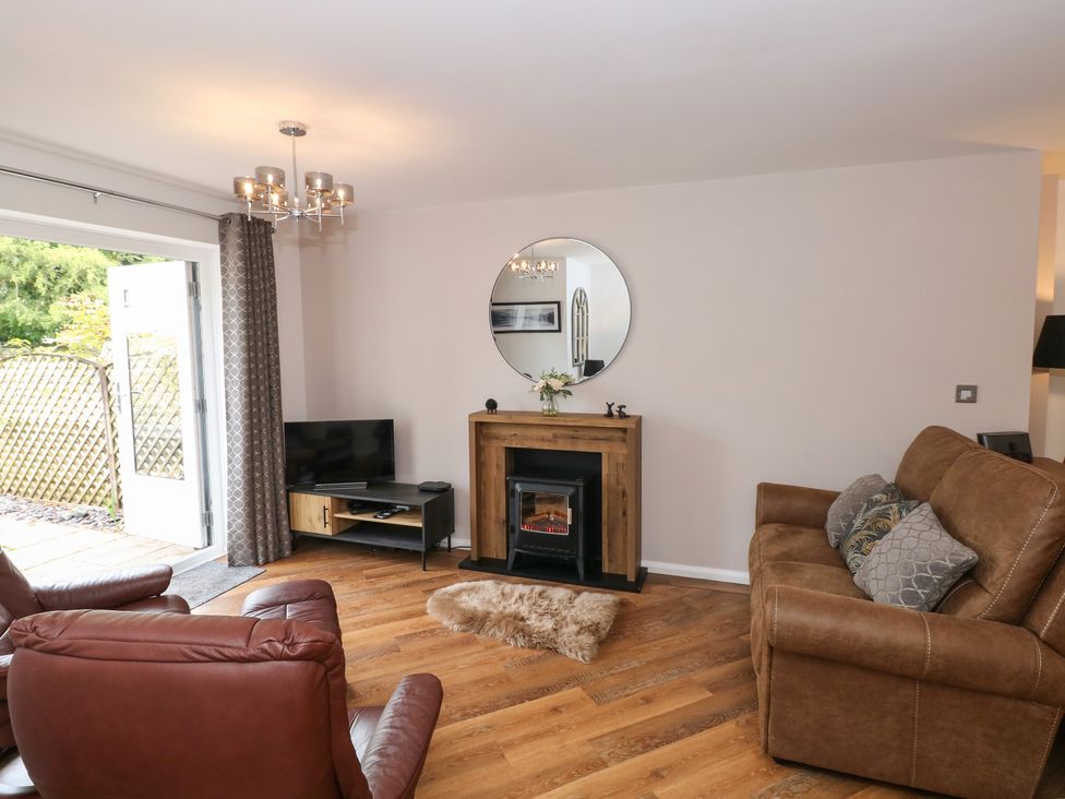 A living room with brown leather chairs a brown sofa a wooden floor a small fireplace a round mirror above the fireplace and a TV on a stand at The Sanctuary in Windermere