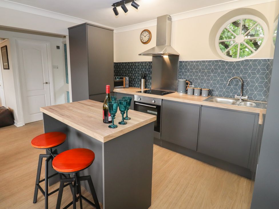 A kitchen with gray cabinets and a wooden island with red stools and three green glasses and a wine bottle at The Grooms in Lydney