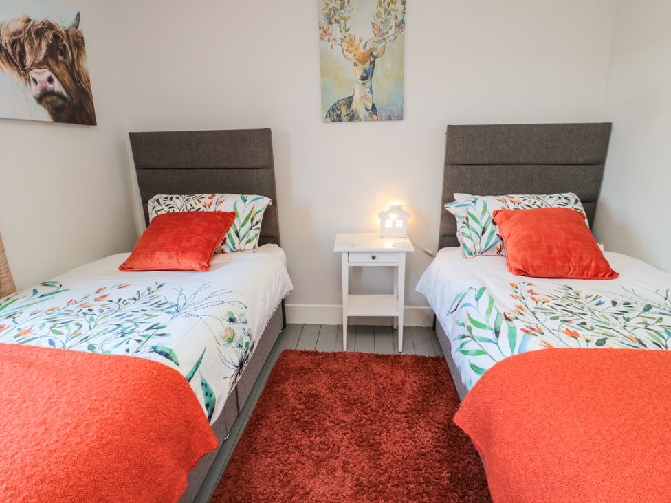A bedroom with two single beds with floral bedding and red pillows a white nightstand with a small house-shaped lamp and animal paintings on the walls at Fox View Cottage in Falstone