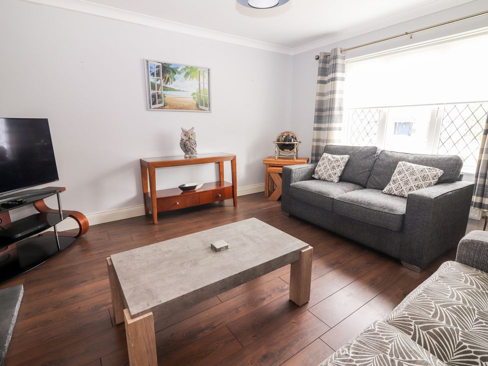 A living room with a grey sofa two patterned cushions wooden floors a coffee table a television and a painting at 17 Clover Hill in Killorglin County Kerry