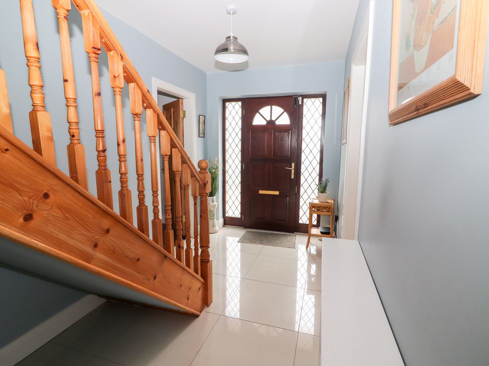 A hallway with a wooden staircase a dark wooden front door and light blue walls at 17 Clover Hill in Killorglin County Kerry