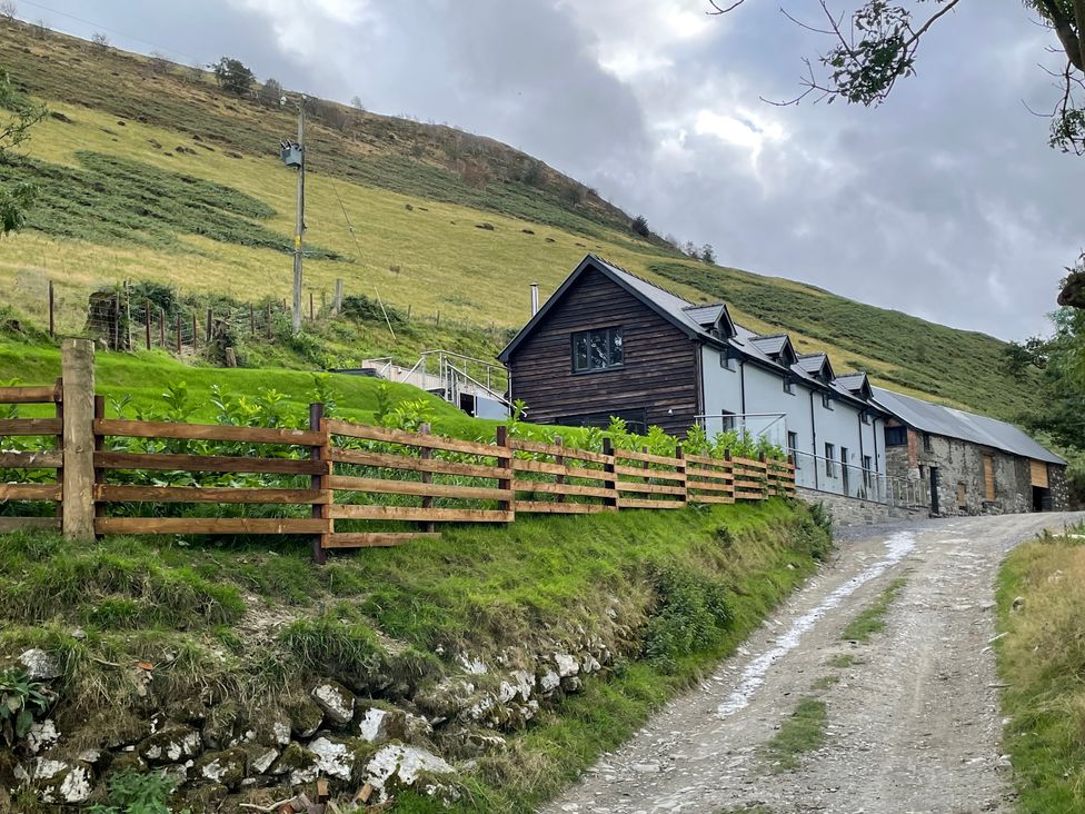 A hillside house with wooden fencing by a gravel road at Pennant Uchaf in Pennant near Llanbrynmair
